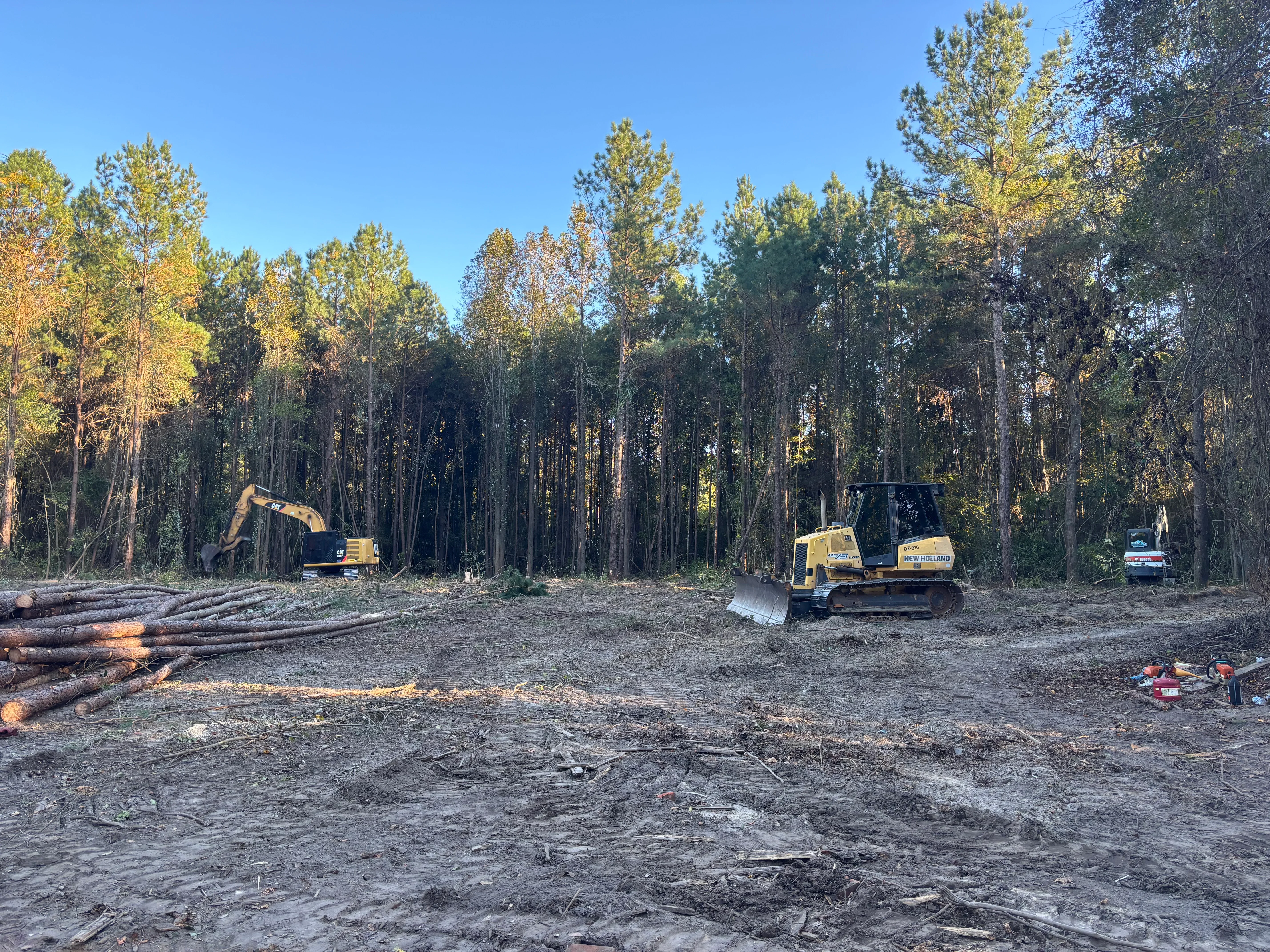 Excavator and dozer clearing forested land with felled logs and prepared soil