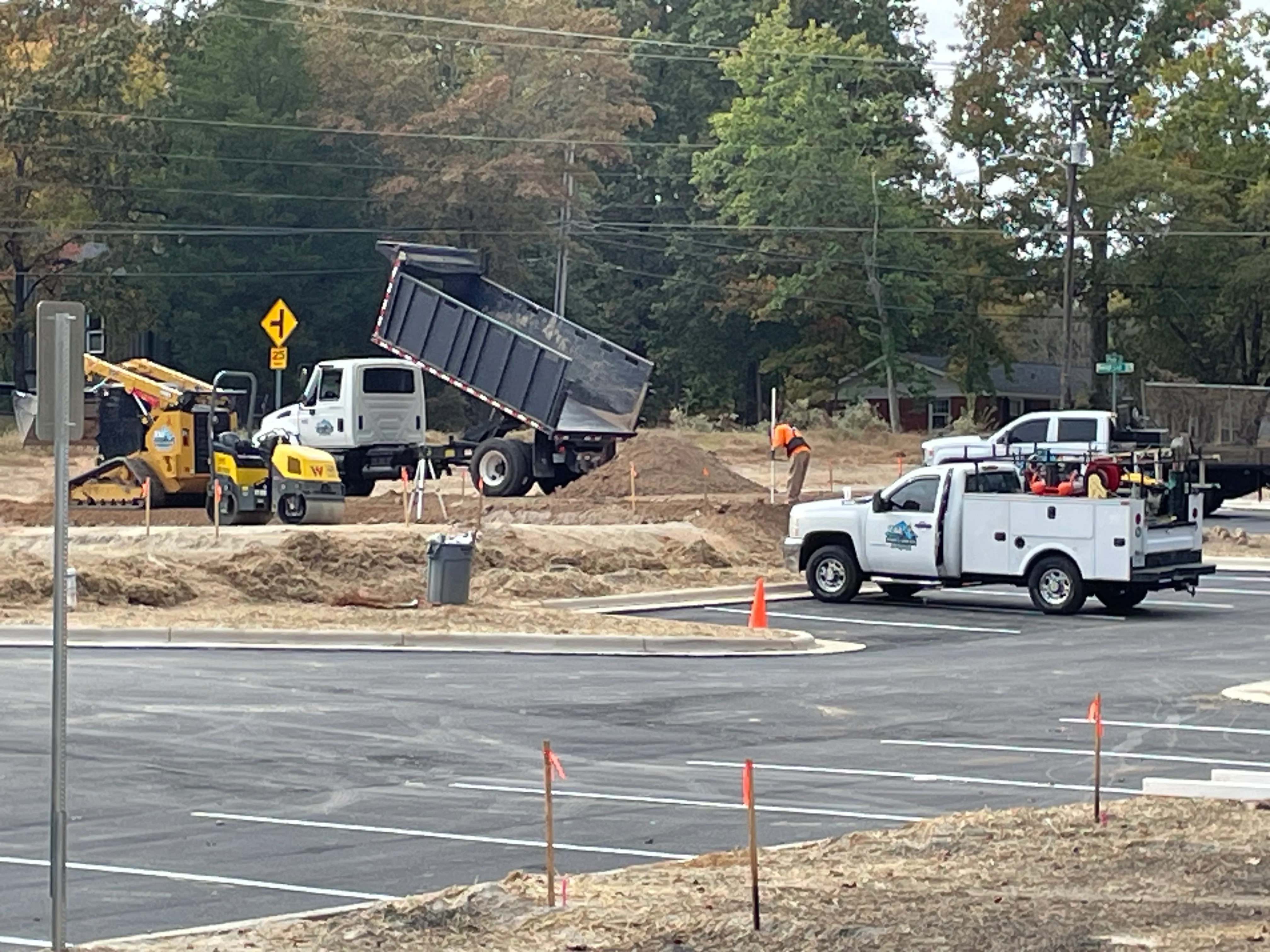 Excavation site with wheel loader, dump truck, and finished asphalt base layer with utility markers