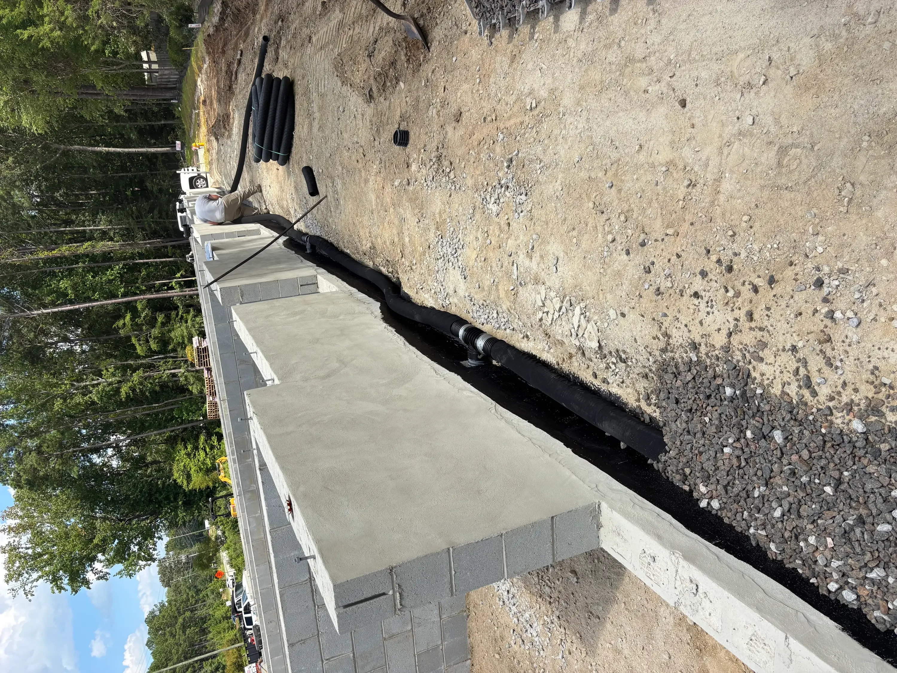 Driveway excavation with black perforated drain pipe, gravel base, and concrete pad installation