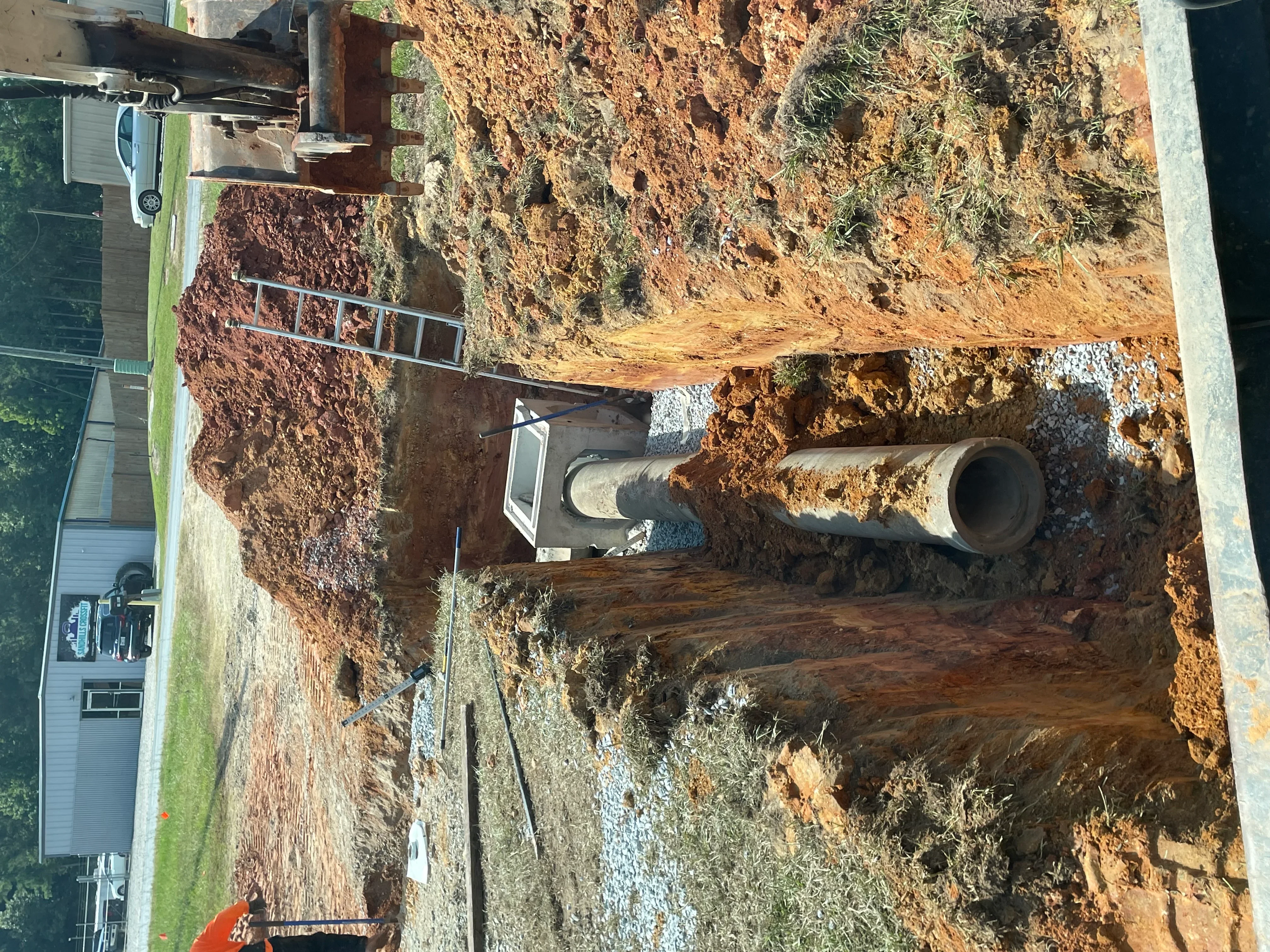 Septic system installation with concrete box, perforated drain pipe, and gravel base in excavated trench
