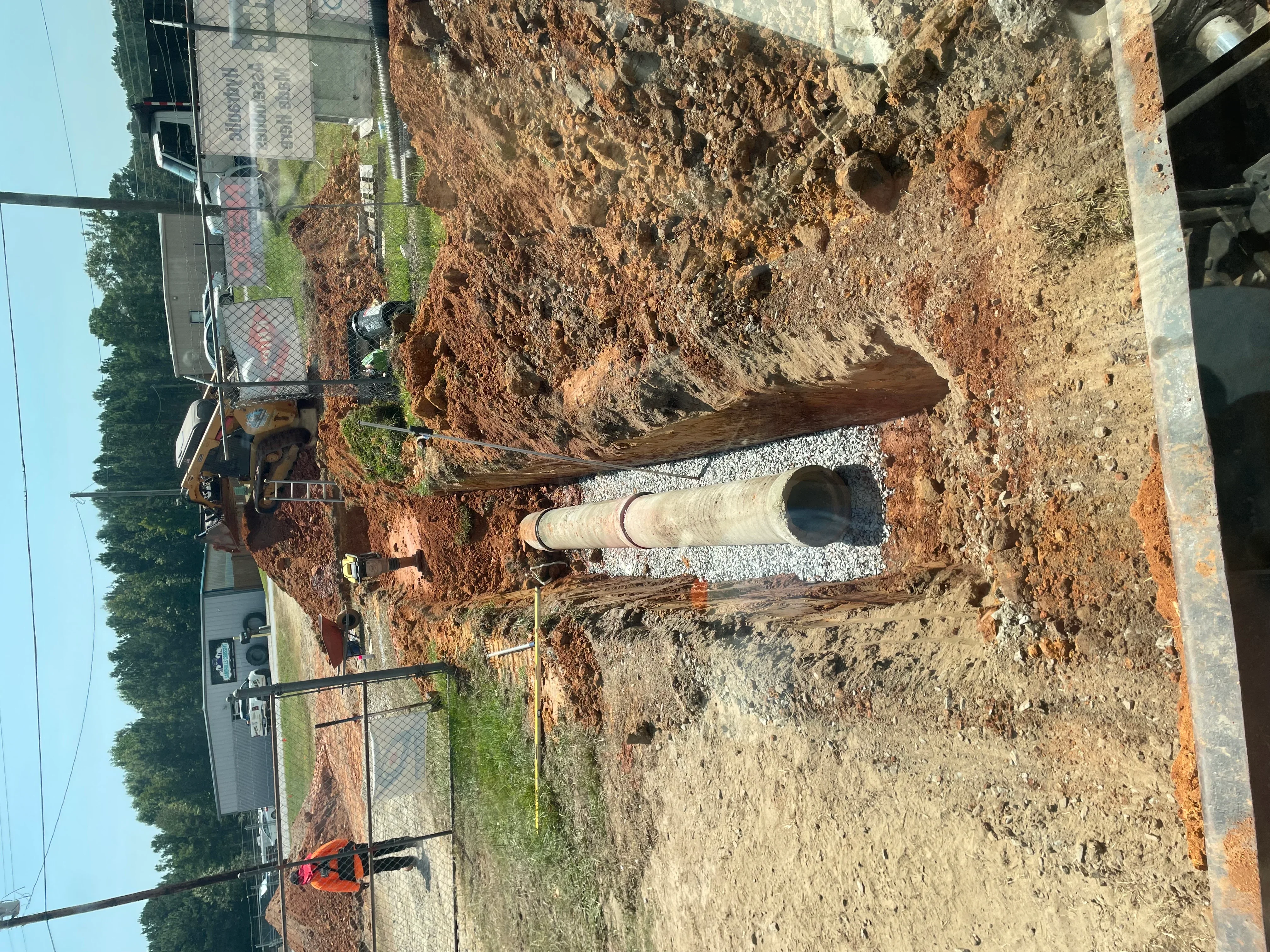 Concrete drainage pipe installed in excavated trench with gravel base and compacted soil