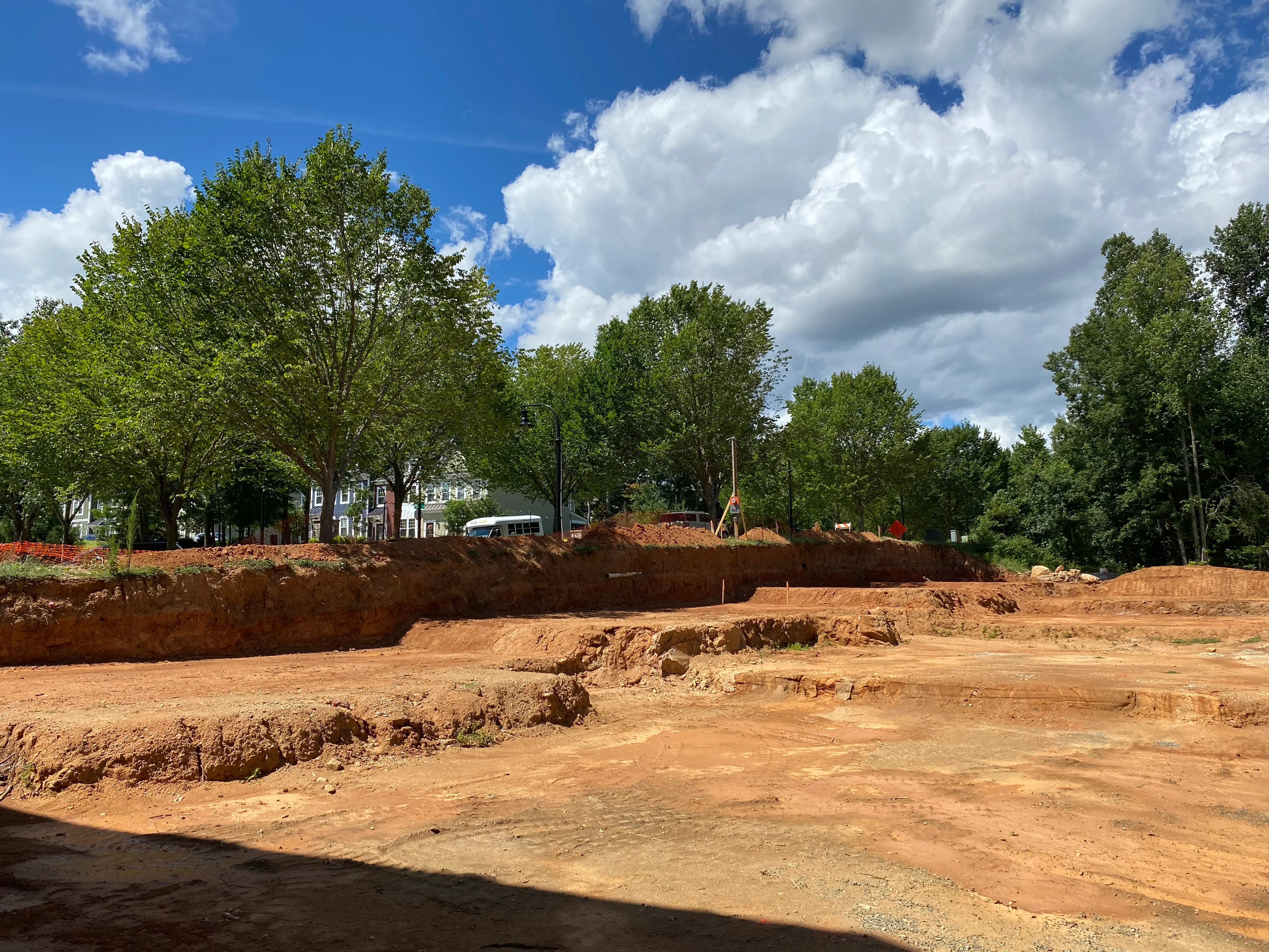 Excavated site with graded soil, cut banks, and mature trees along property edge