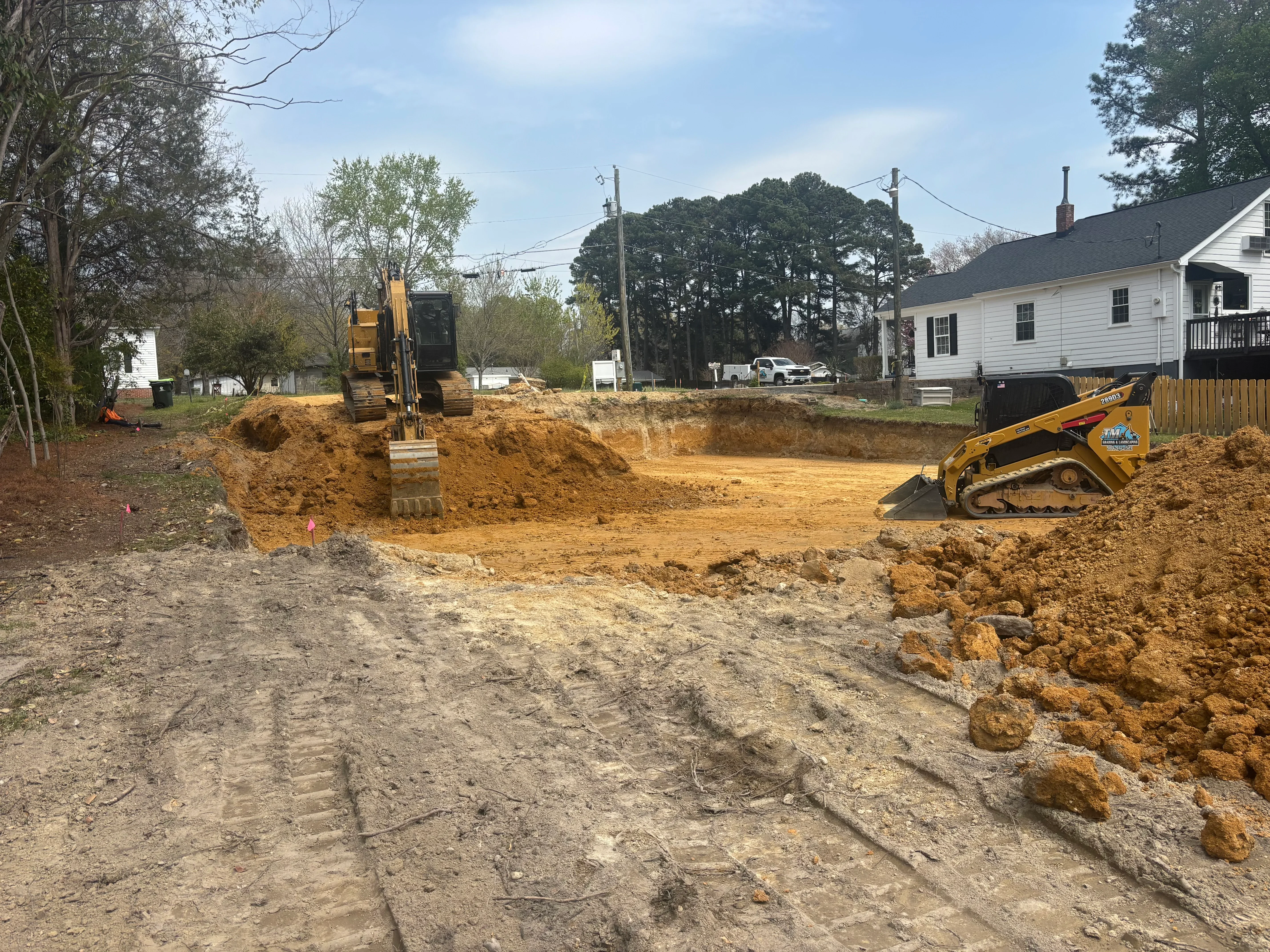 Tracked excavator and skid steer loader grading clay soil on residential property