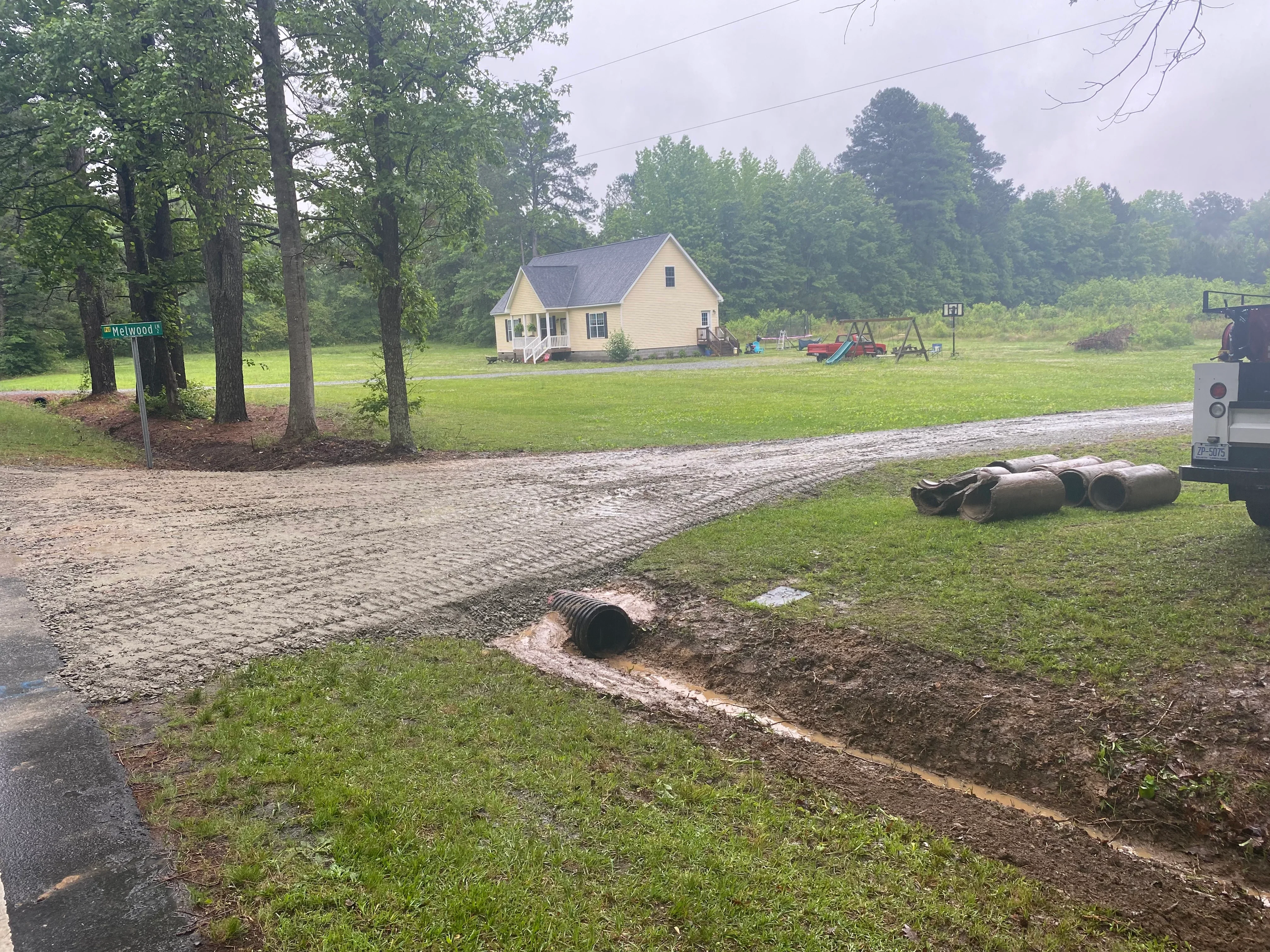 Corrugated metal drainage pipe installation with excavated trench and gravel driveway base