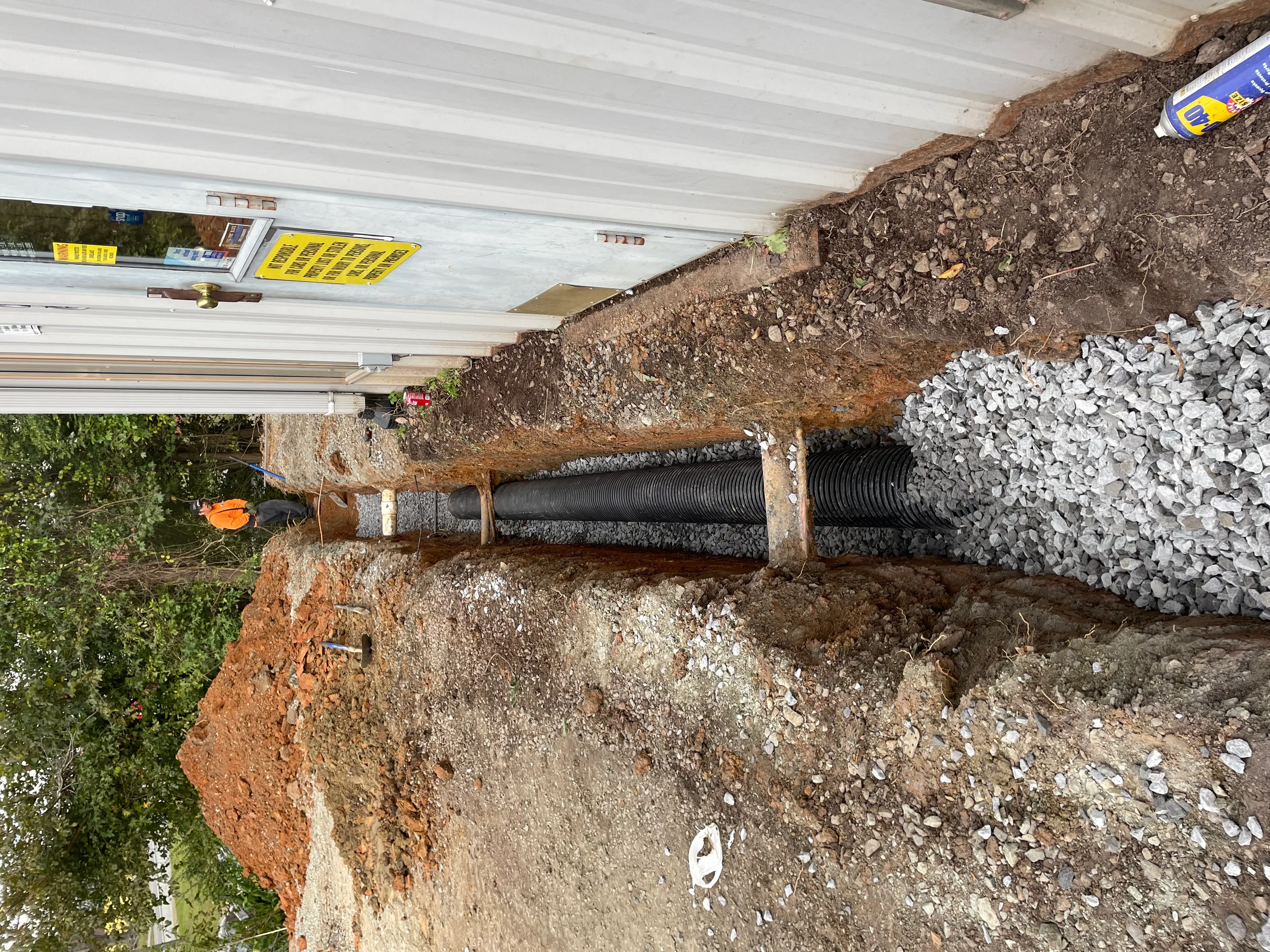 Corrugated drainage pipe installation in excavated trench with gravel base and stone backfill materials