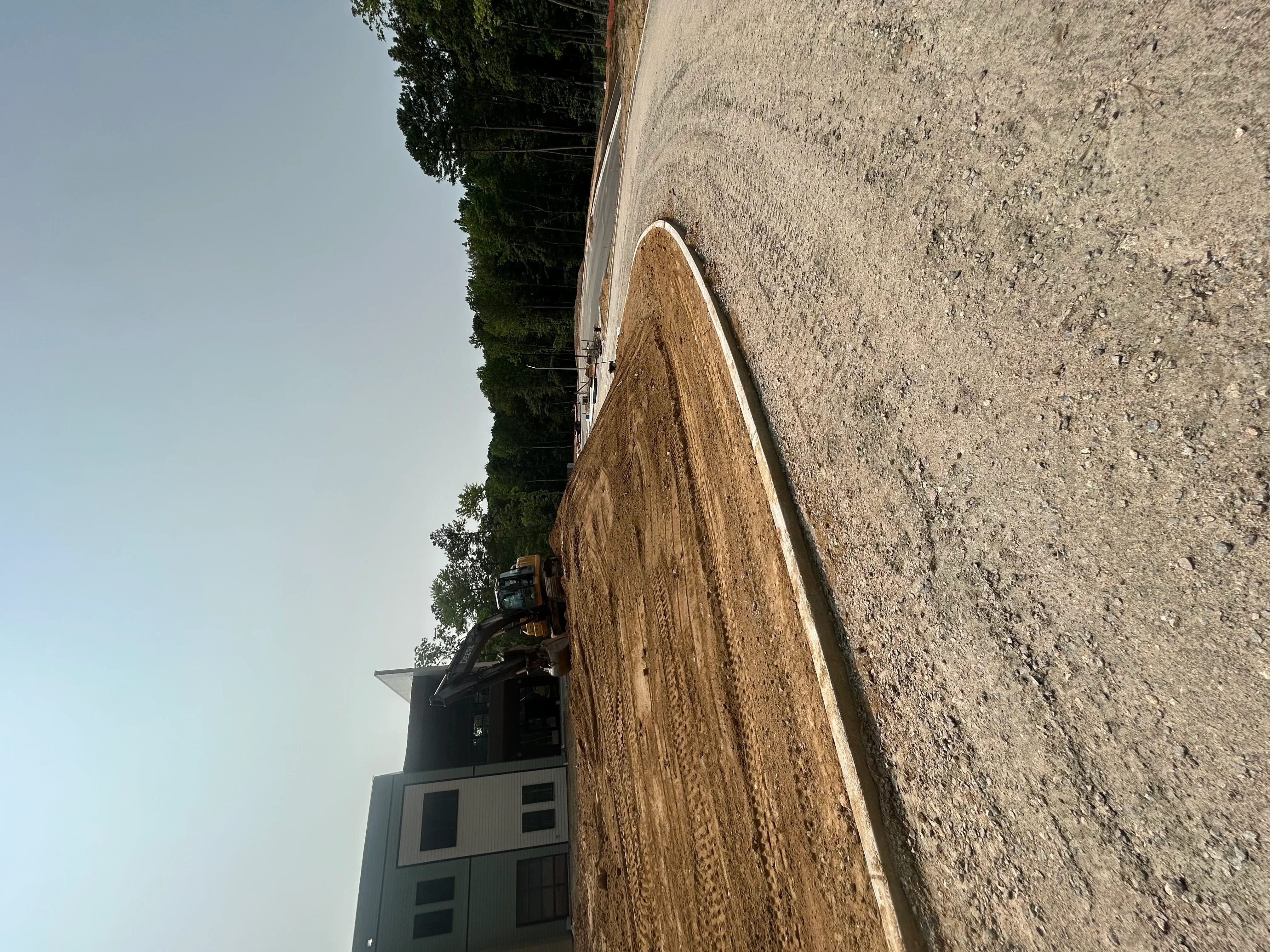 Newly graded driveway with concrete apron and white edge trim, adjacent to residential structure