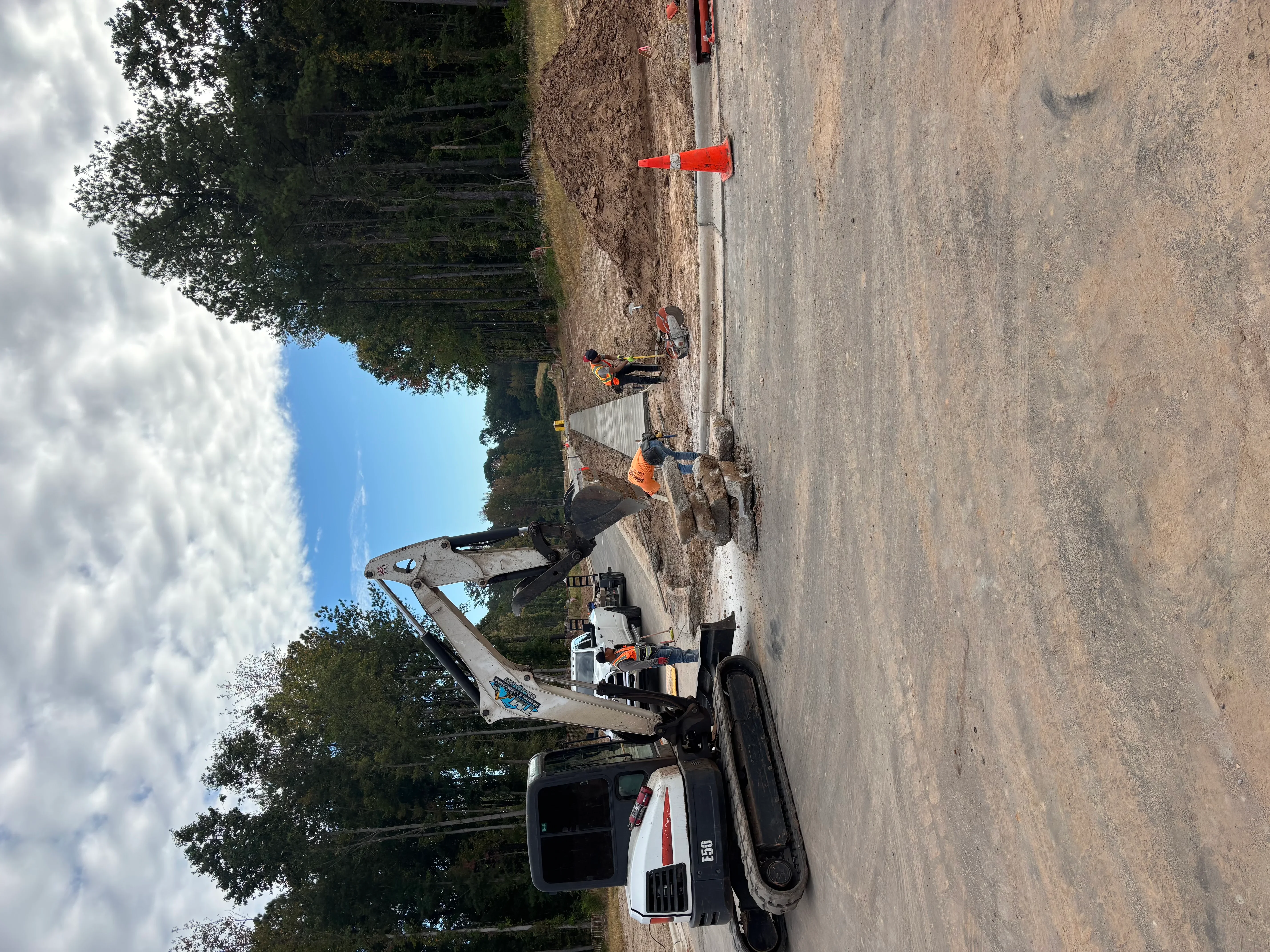 Compact excavator grading driveway site with crew members and survey equipment