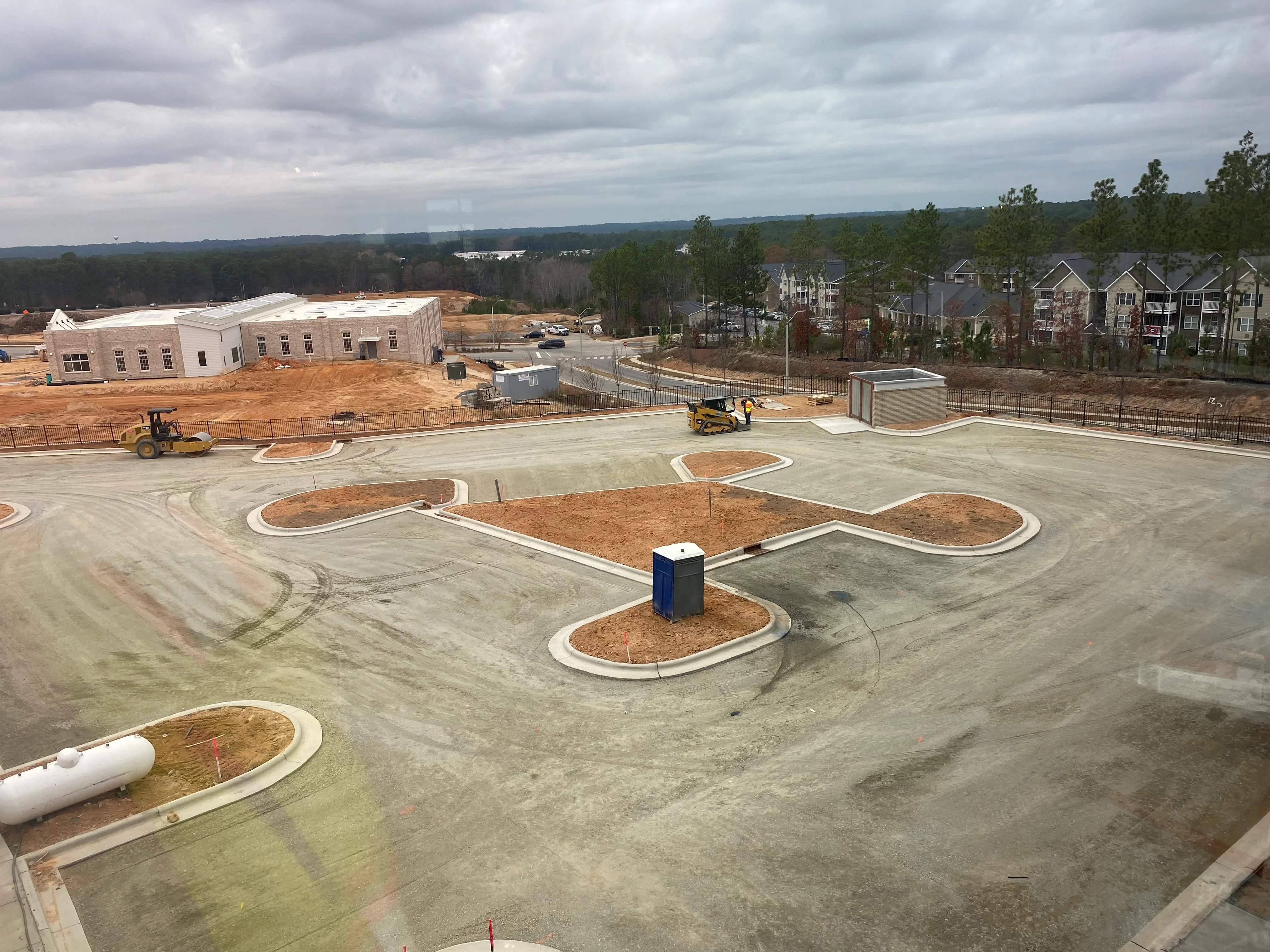 Concrete park pathways with landscaped planting beds, grading equipment, and utility structures under construction