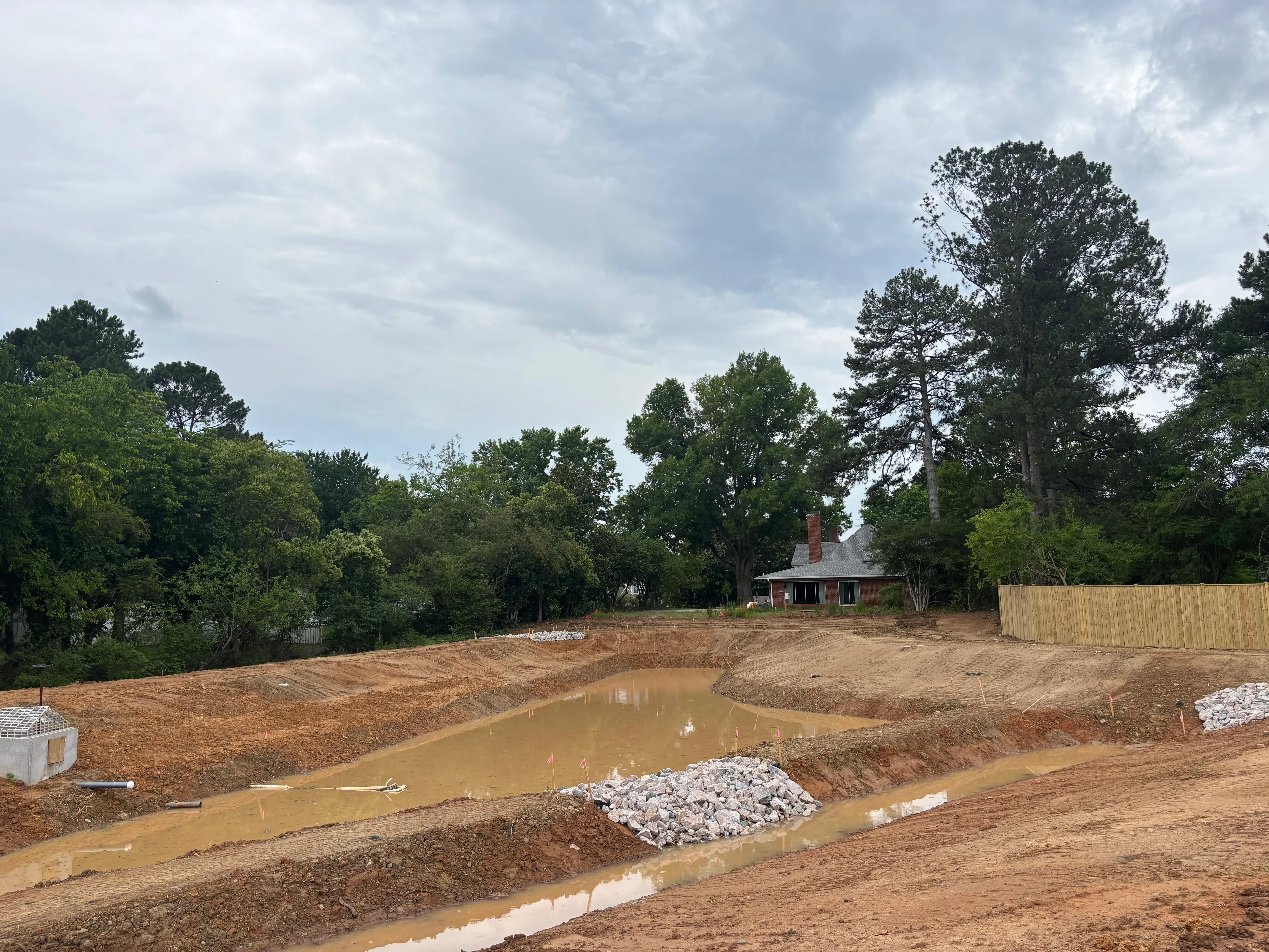 Excavated residential lot with drainage channels, compacted soil, and stone aggregate during grading work