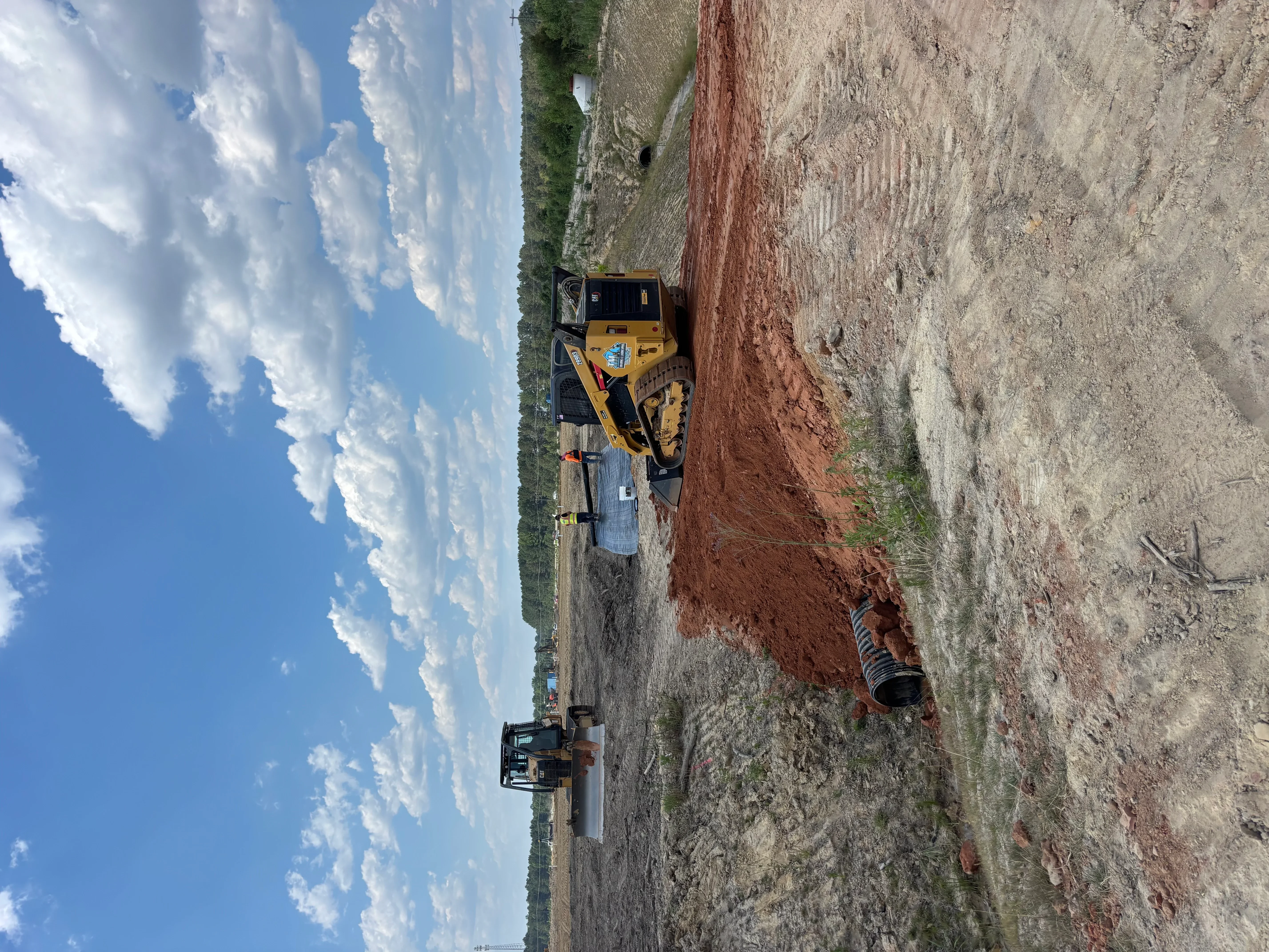 Compact track loader excavating and grading driveway base with red clay soil visible