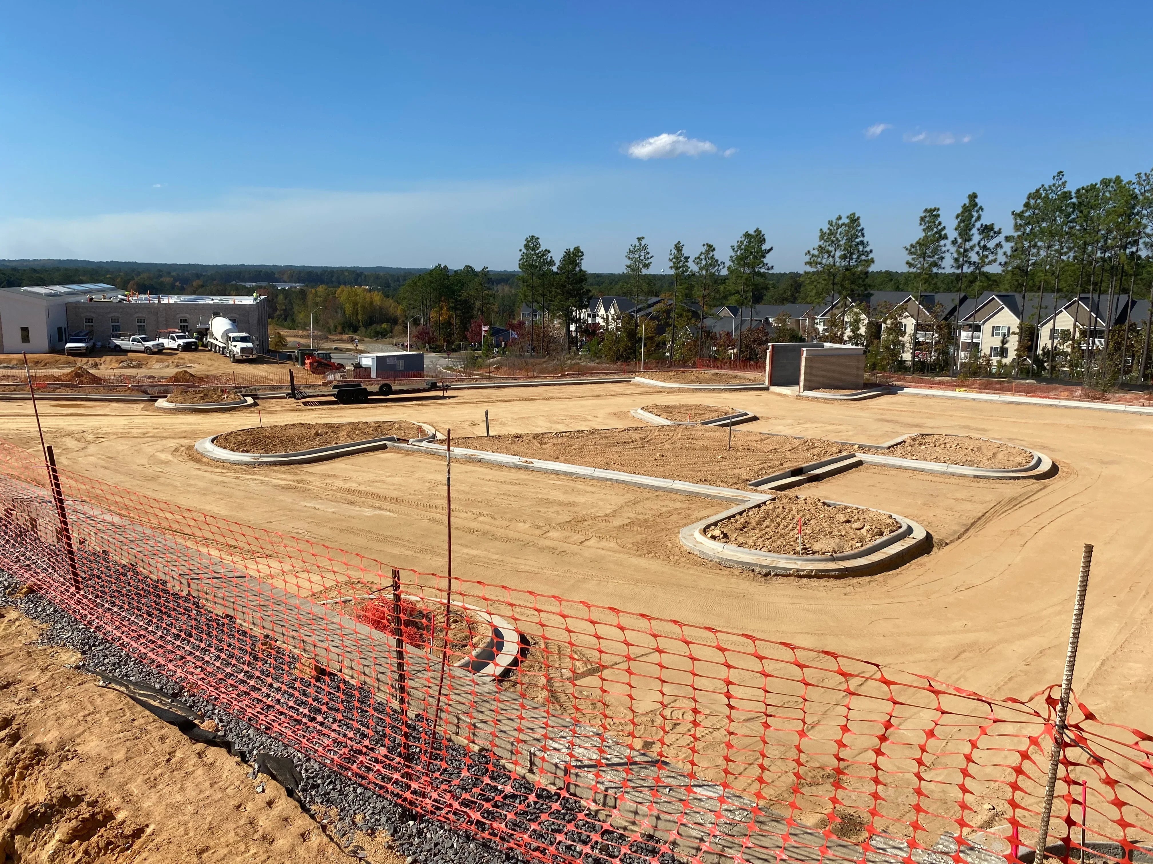 Graded residential lots with concrete curbing, compacted soil, and red erosion control fencing