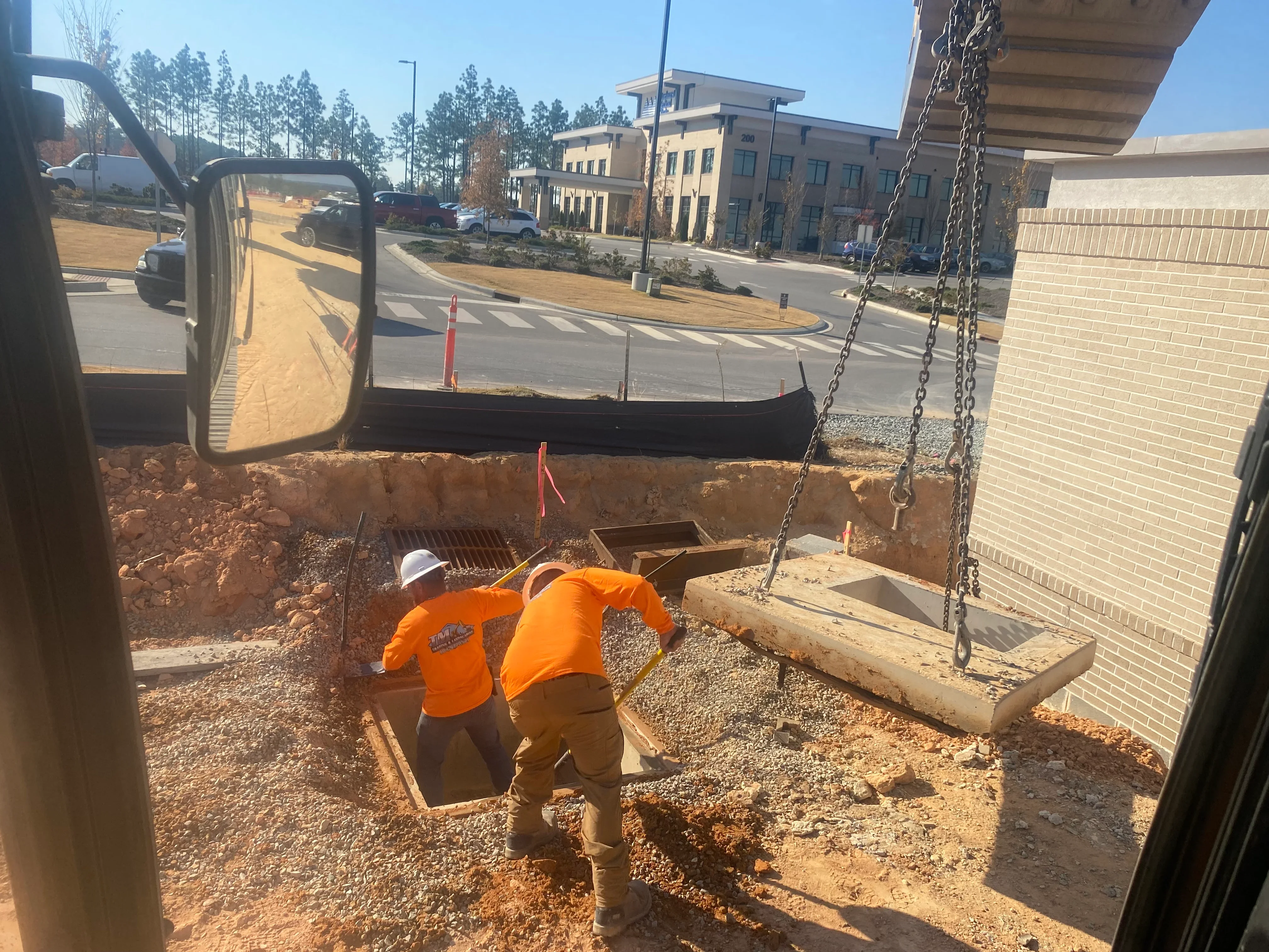 Excavation crew in orange vests working on deep site grading with concrete drainage box and heavy equipment