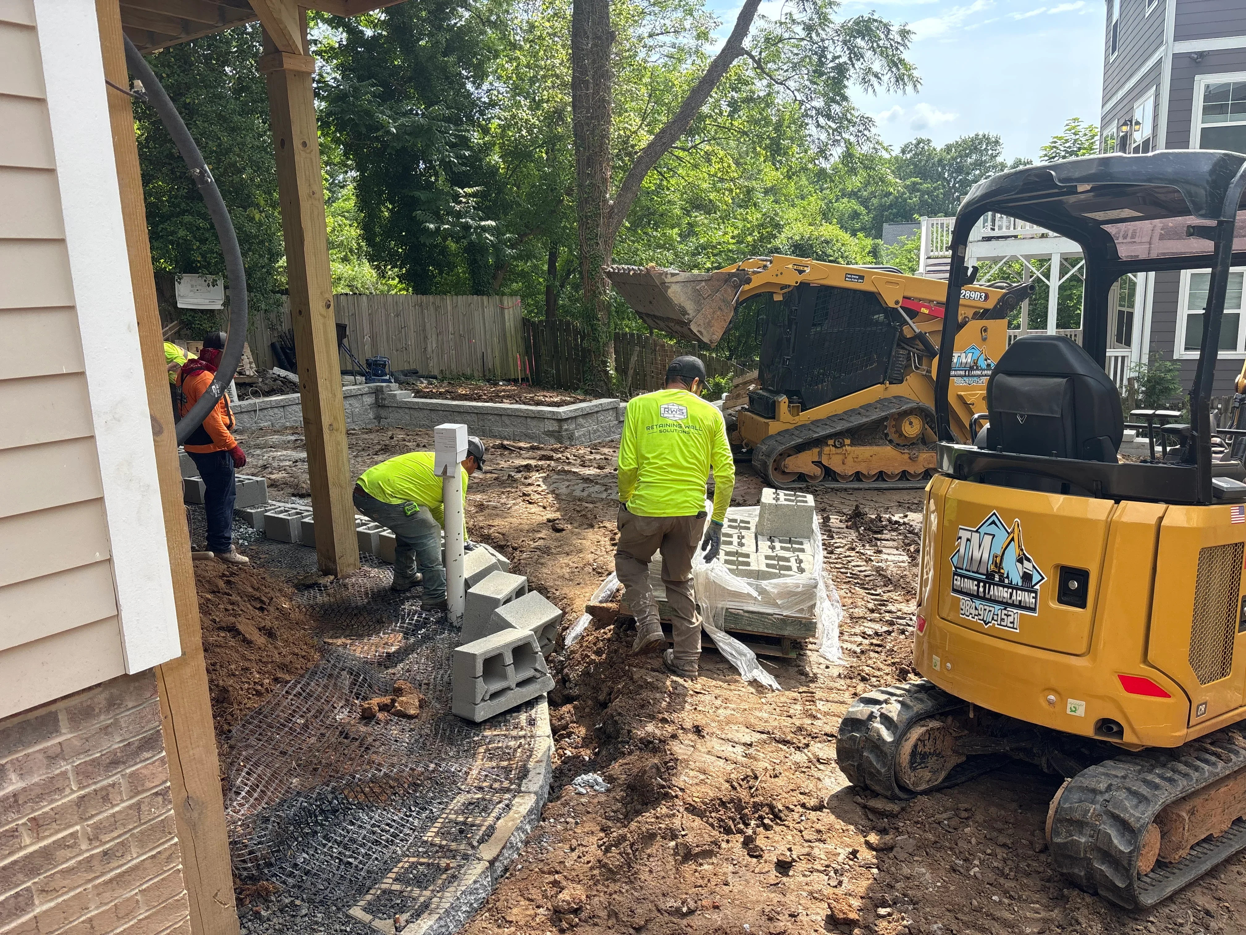 Excavation crew installing concrete piers and landscape fabric during residential grading work