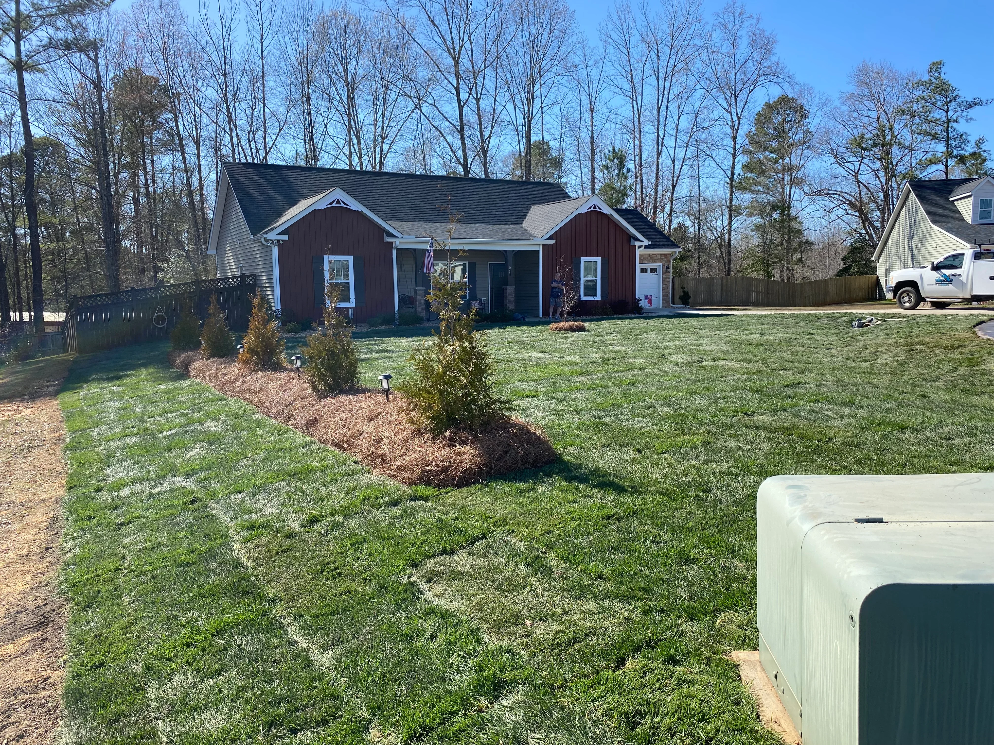 Newly graded lawn with sod, mulched planting beds, and evergreen shrubs around residential home