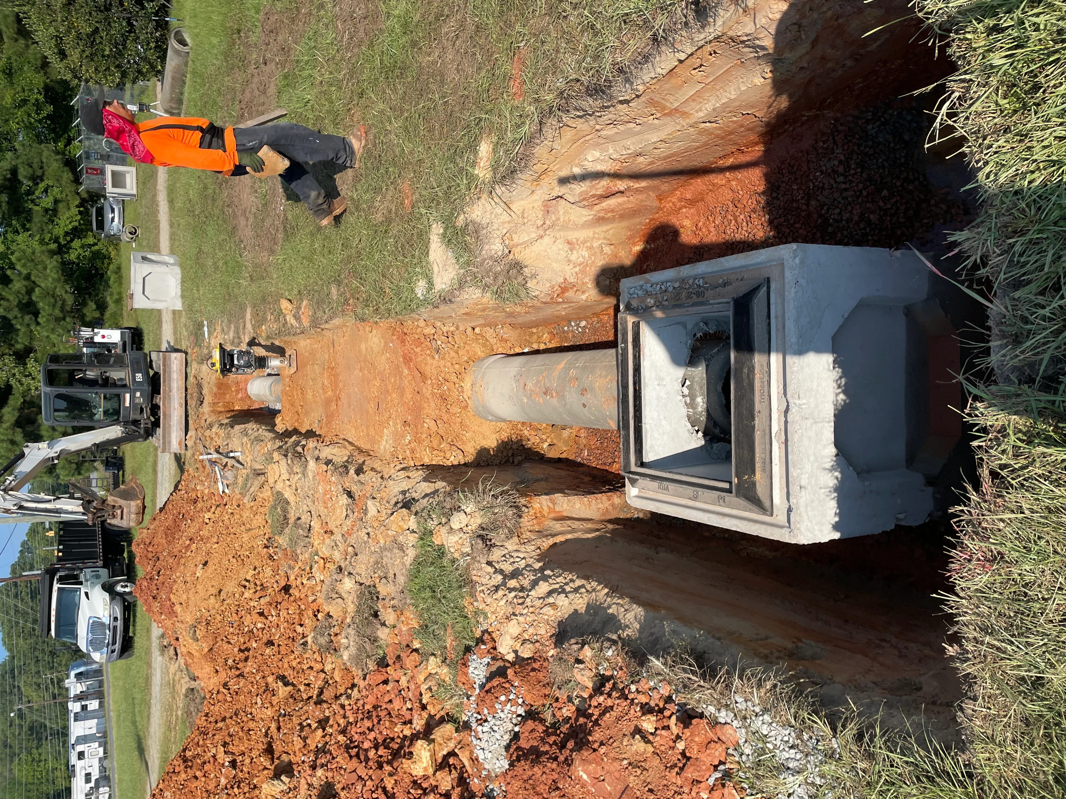 Septic tank installation with concrete tank, excavated red clay soil, and underground piping connections