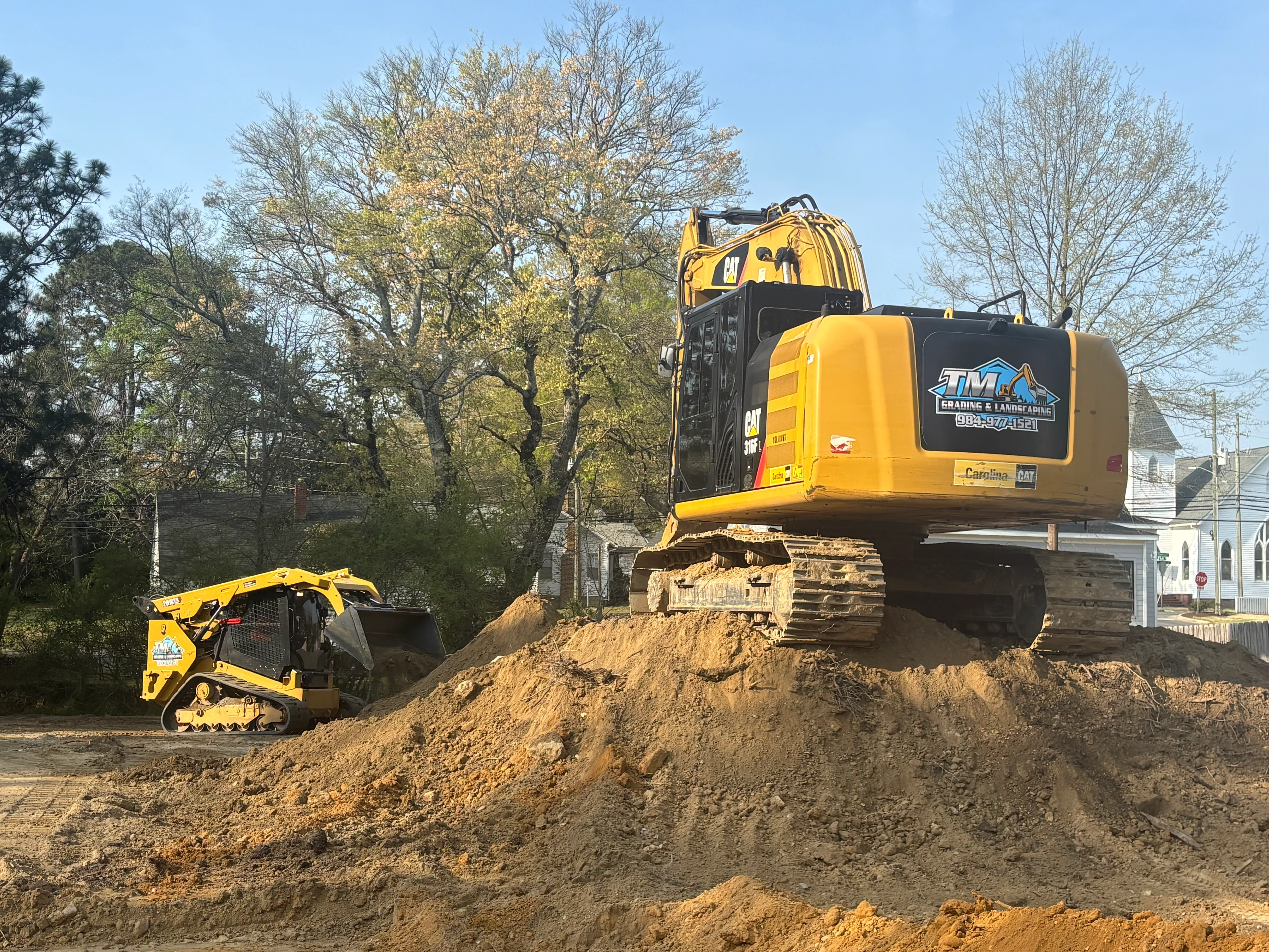 CAT excavator and compact track loader moving soil during residential site excavation and grading