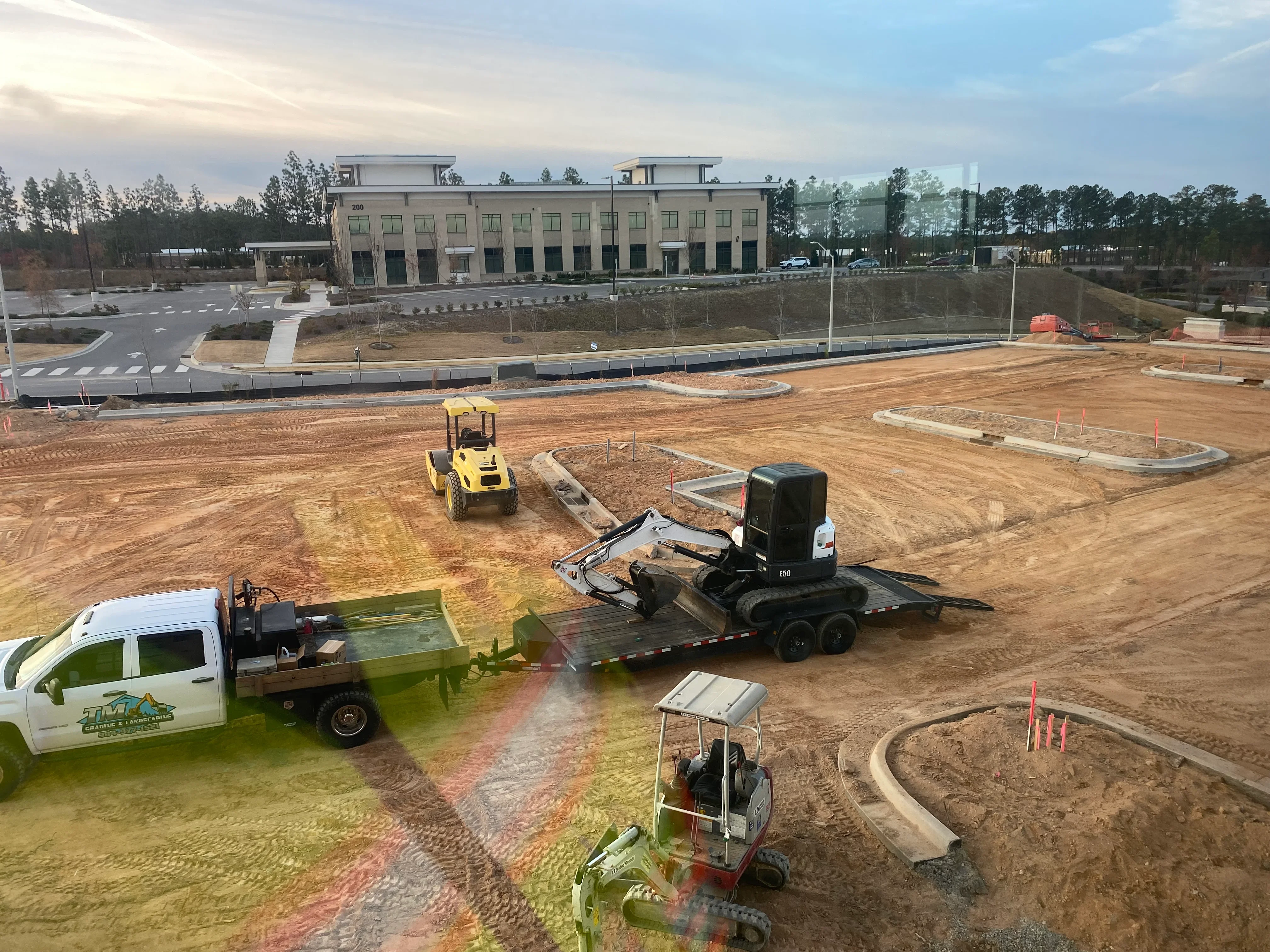 Excavation equipment grading commercial building site with concrete curbing and drainage installation