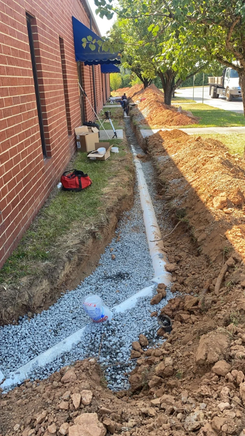 Trench with PVC drainage pipe and gravel base along brick building foundation