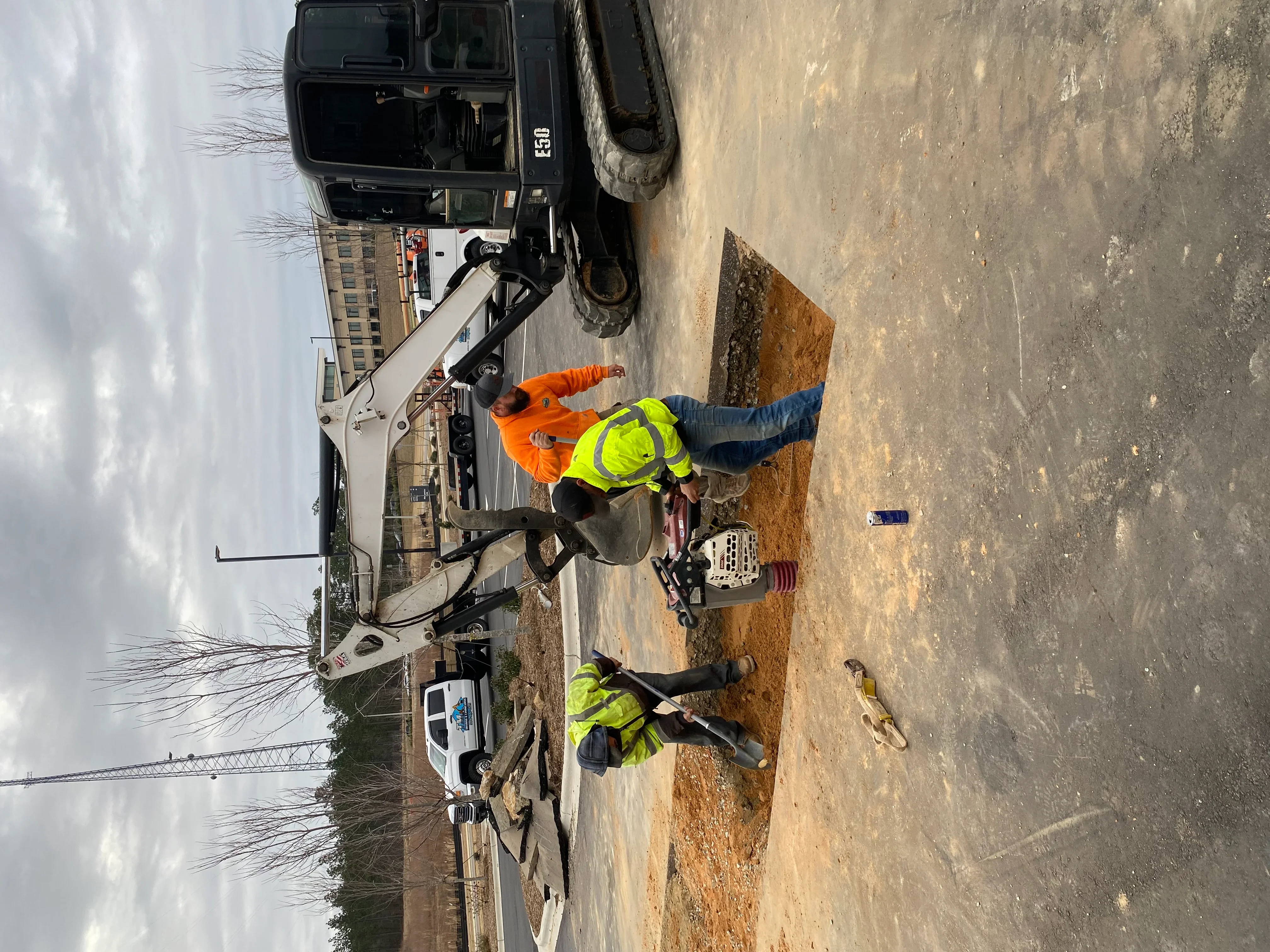 Mini excavator grading bare earth site with crew in safety vests
